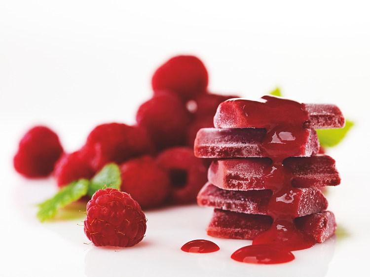 Fryst hallonpuré som börjar smälta och färska hallon i bakgrunden