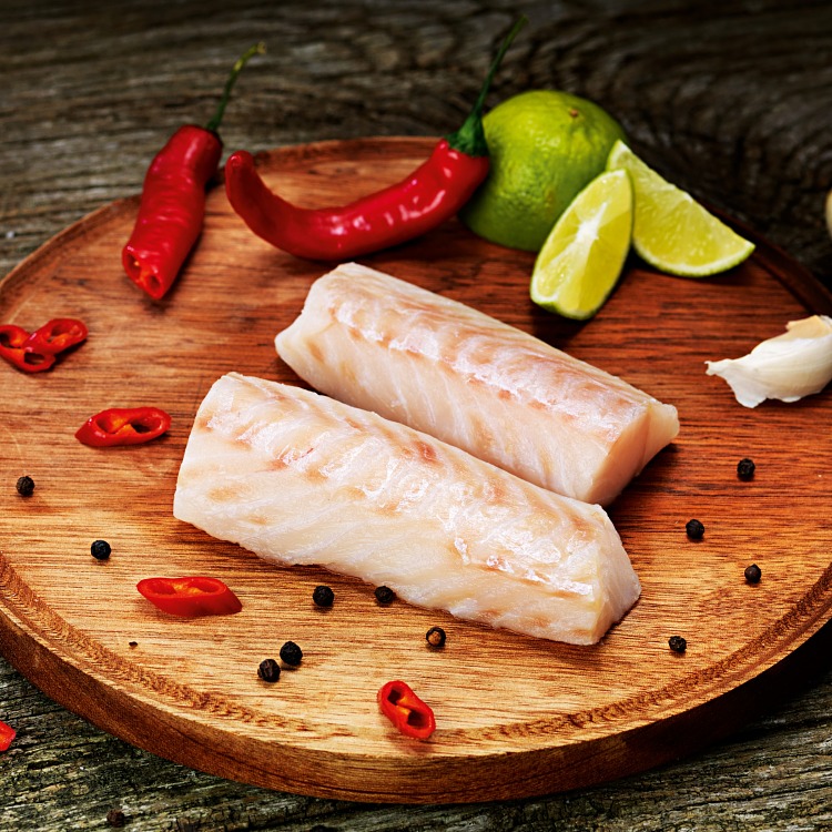 Ryggbitsfilé av torsk på en runt skärbräda med chili och lime